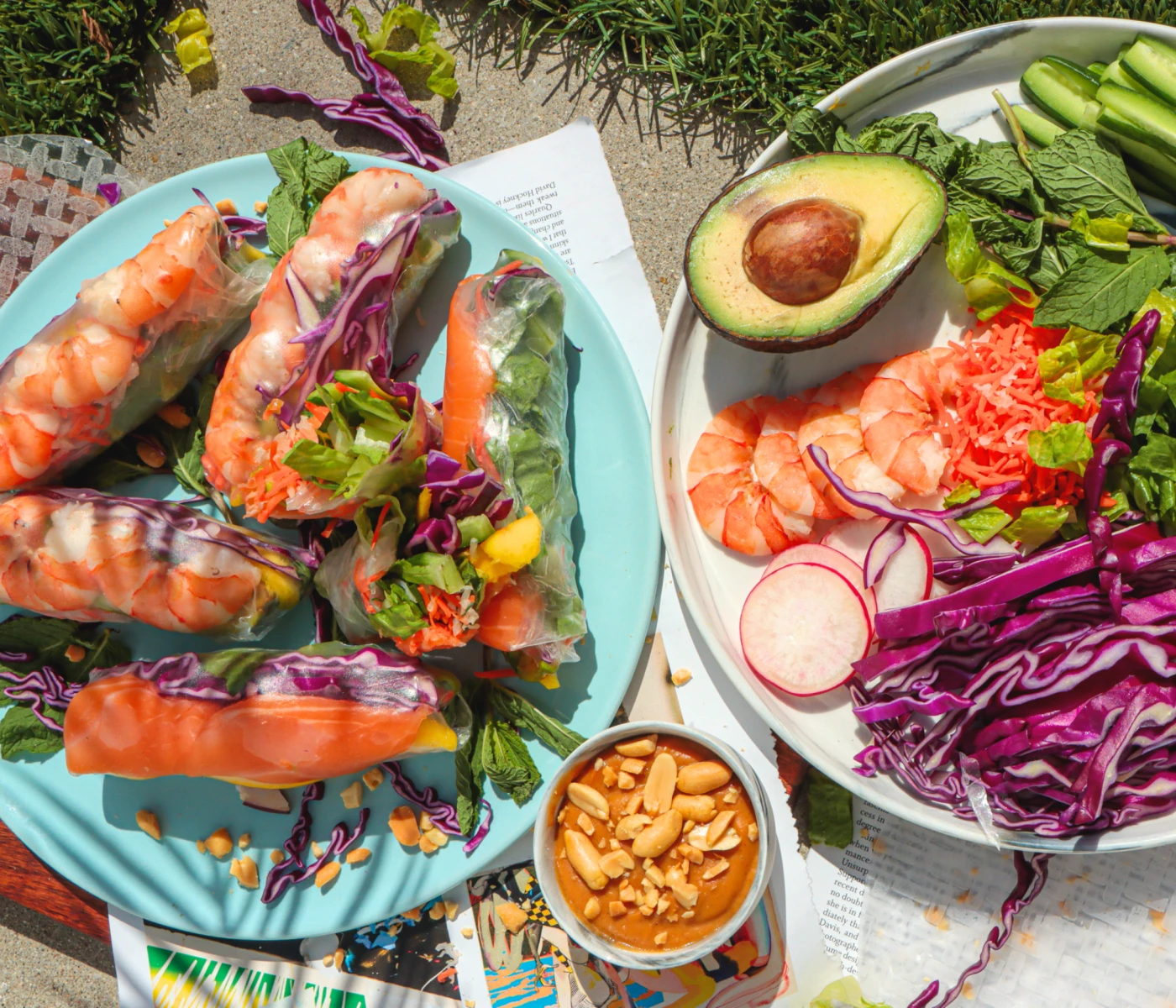 Colorful shrimp spring rolls with a peanut sauce and raw ingredients.