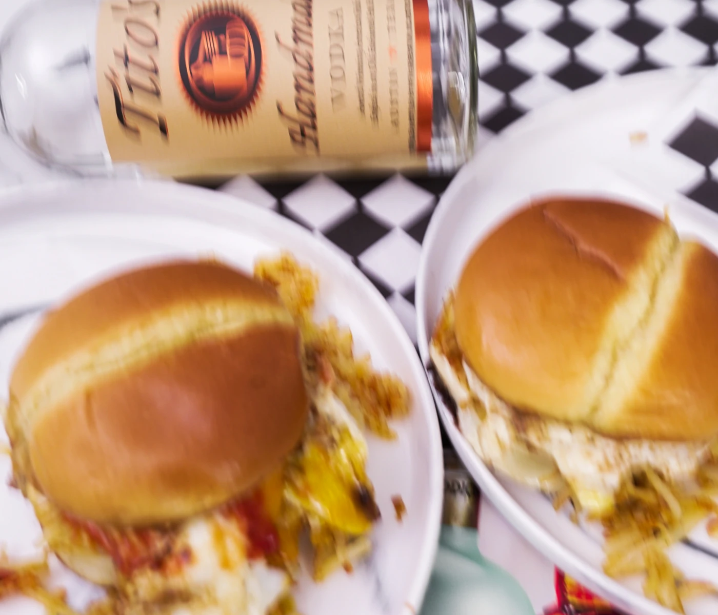 Blurry photo of loaded breakfast burgers and a Tito's bottle in the background.